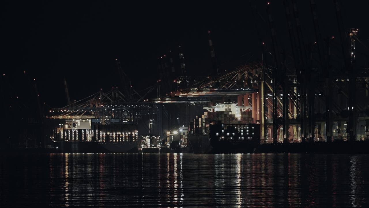 Container port cranes lit at night, reflected in the water